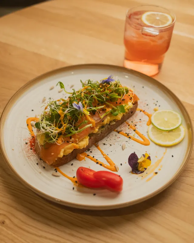 Toast topped with scrambled eggs, smoked salmon, microgreens, and a drizzle of sauce, served with le