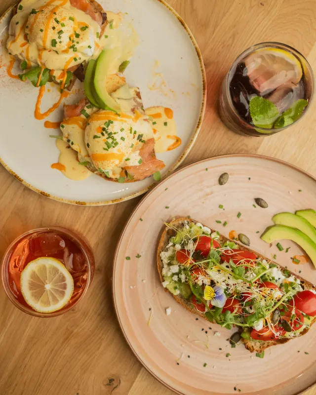 Benedict with salmon, poached eggs, and hollandaise sauce, garnished with chives and avocado slices.